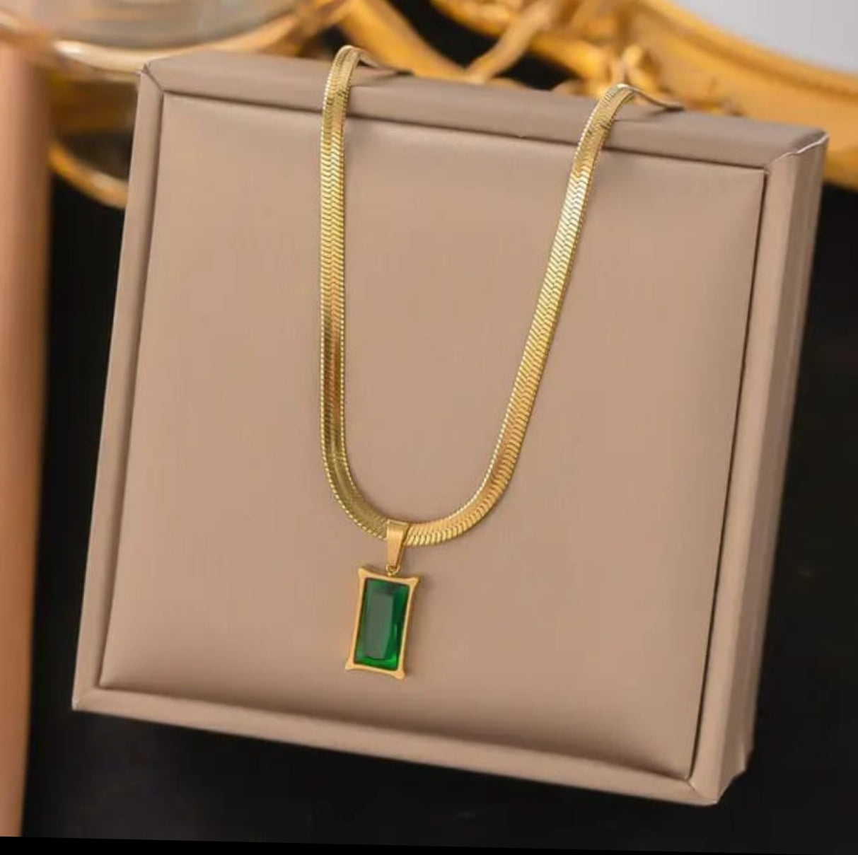 Gold chain necklace with a rectangular green gemstone pendant.